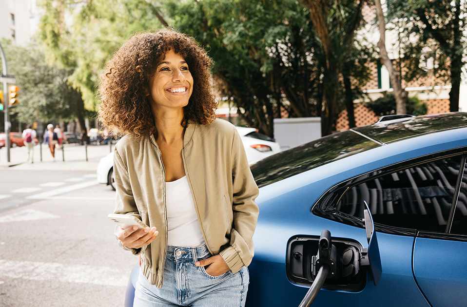 Mujer junto a un vehículo eléctrico mientras se carga.